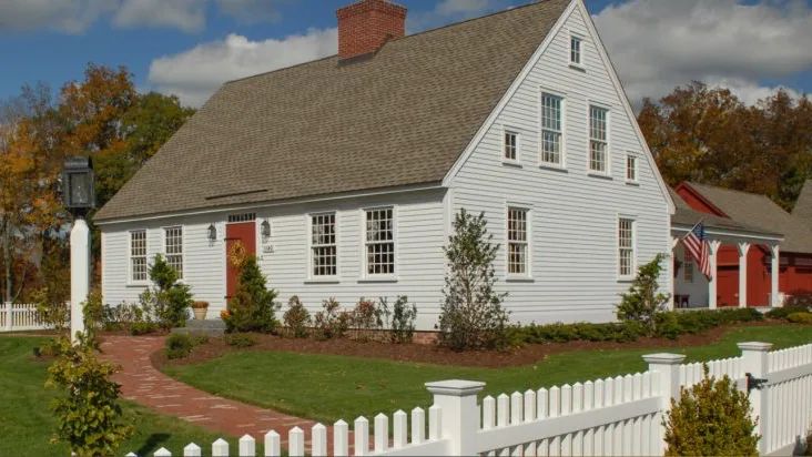 White colonial home with a picket fence and brick walkway